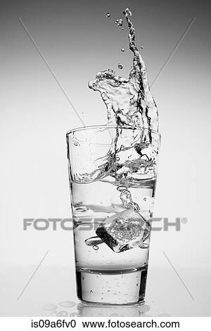 Stock Image - Ice cube falling into glass of water. Fotosearch