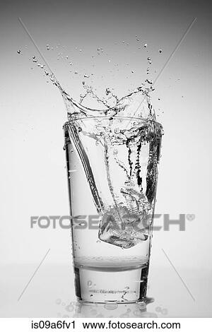 Stock Image - Ice cube falling into glass of water. Fotosearch