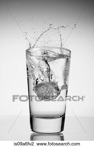 Stock Image - Ice cube falling into glass of water. Fotosearch
