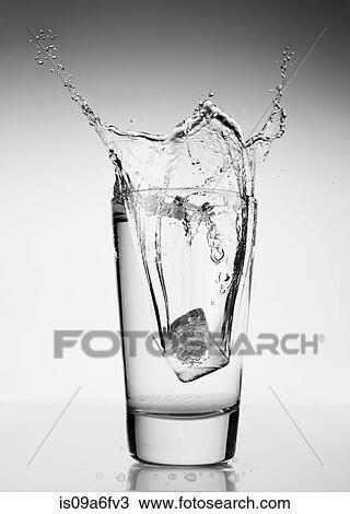 Stock Image - Ice cube falling into glass of water. Fotosearch