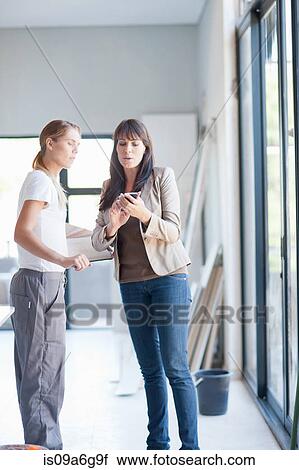 Stock Image - Interior designer and laborer looking at smartphone. Fotosearch
