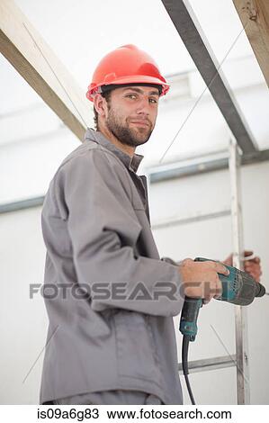 Male laborer on ladders with electric drill on construction site View Large Photo Image Stock Image - Male laborer on ladders with electric drill on construction site. Fotosearch