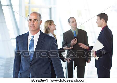 Stock Image - Mature businessman with colleagues in background. Fotosearch