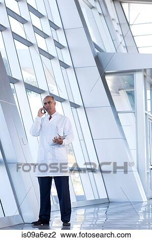 Stock Image - Mature male doctor on cell phone. Fotosearch