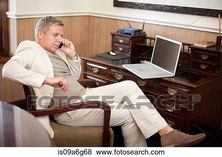 Mature man on cell phone sitting at desk View Large Photo Image Stock Photo - Mature man on cell phone sitting at desk. Fotosearch