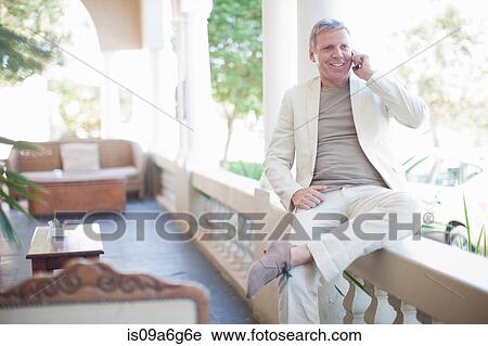 Stock Image - Mature man sitting on wall on smartphone. Fotosearch