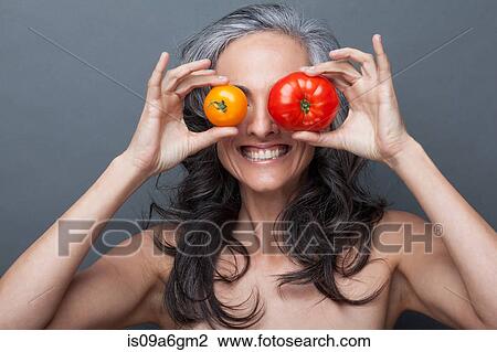 Stock Image - Mature woman covering eyes with red and yellow tomato. Fotosearch