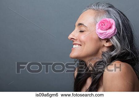 Stock Photograph - Mature woman with pink flower in hair, eyes closed. Fotosearch
