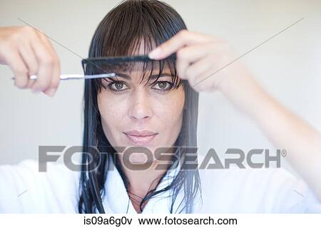 Stock Photo - Mid adult woman cutting her own fringe. Fotosearch