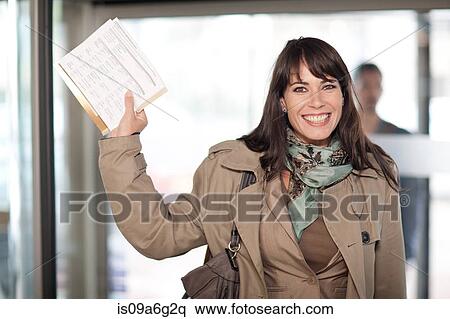 Stock Photography - Mid adult woman smiling holding up paperwork. Fotosearch