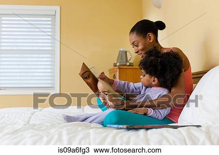 Stock Image - Mother and daughter reading in bed. Fotosearch