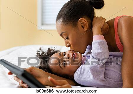 Mother kissing daughter and holding digital tablet View Large Photo Image Stock Photograph - Mother kissing daughter and holding digital tablet. Fotosearch