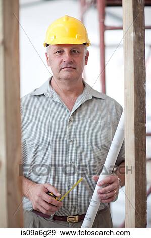 Portrait of a builder with tape measure and blueprint on construction site View Large Photo Image Stock Photo - Portrait of a builder with tape measure and blueprint on construction site. Fotosearch