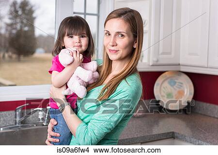 Portrait of mother holding toddler daughter in kitchen View Large Photo Image Picture - Portrait of mother holding toddler daughter in kitchen. Fotosearch