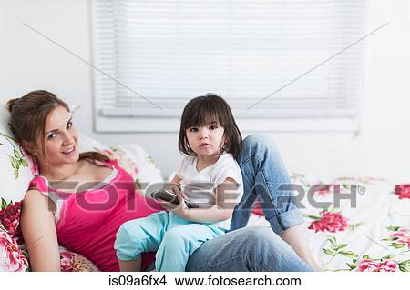 Picture - Portrait of pregnant woman and toddler daughter lounging on bed with smartphone. Fotosearch