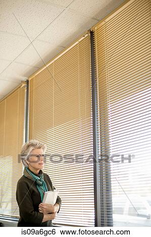 Stock Photograph - Senior woman looking through window. Fotosearch