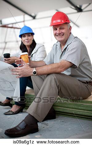 Smiling male and female construction workers sitting down holding coffee and a blueprint View Large Photo Image Stock Photo - Smiling male and female construction workers sitting down holding coffee and a blueprint. Fotosearch
