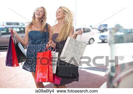 Picture - Two happy young women carrying shopping bags. Fotosearch