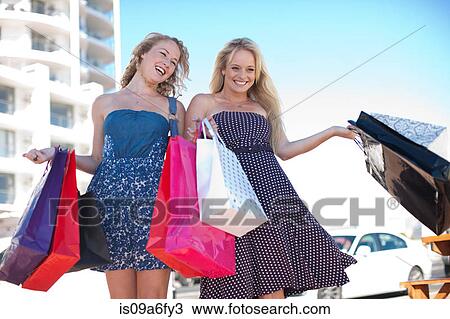 Two happy young women carrying shopping bags View Large Photo Image Stock Image - Two happy young women carrying shopping bags. Fotosearch