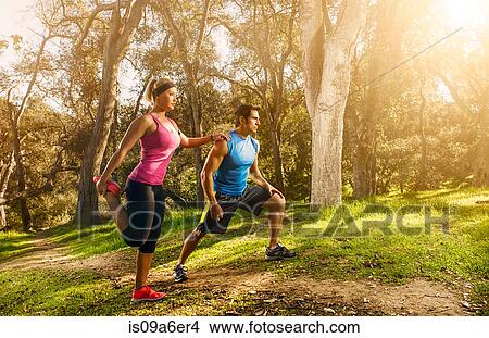 Picture - Two people exercising in forest doing warm up stretches. Fotosearch