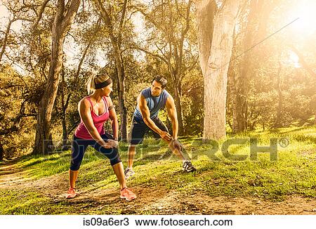 Stock Image - Two people exercising in forest doing warm up stretches. Fotosearch