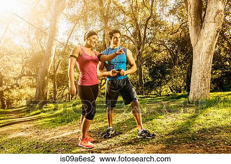 Stock Image - Two people exercising in forest deciding on direction. Fotosearch