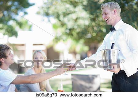 Stock Image - Waiter serving customers in garden. Fotosearch