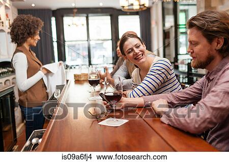 Picture - Woman and man at bar chatting and checking cell phone. Fotosearch