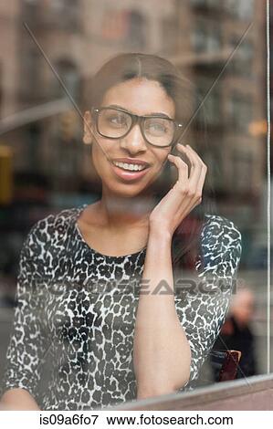 Stock Photo - Woman looking out of window talking on cell phone. Fotosearch