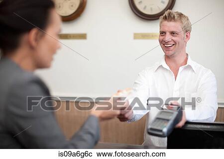Stock Image - Woman paying young man on hotel reception. Fotosearch