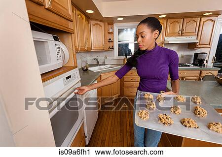 Stock Image - Woman putting tray of cookies into oven. Fotosearch