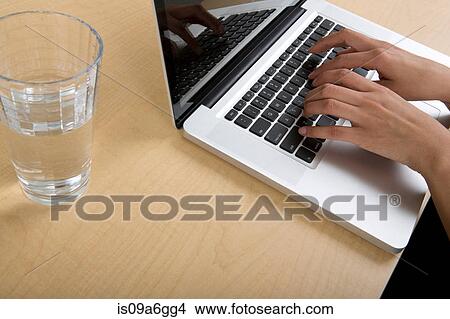 Picture - Woman using laptop with glass of water. Fotosearch