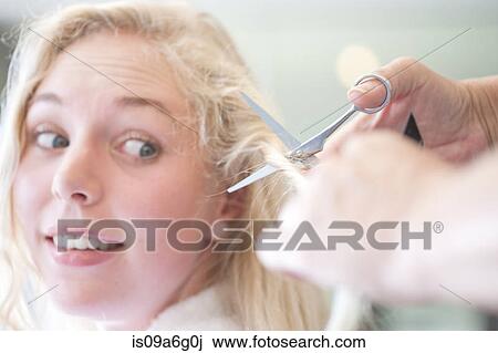 Stock Image - Worried young woman having haircut. Fotosearch