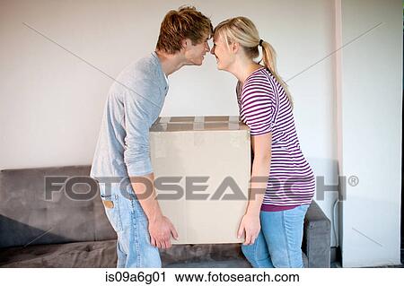 Stock Image - Young couple moving house carrying box. Fotosearch