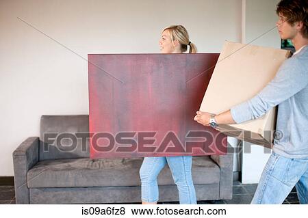 Young couple moving house carrying box and painting View Large Photo Image Stock Photo - Young couple moving house carrying box and painting. Fotosearch
