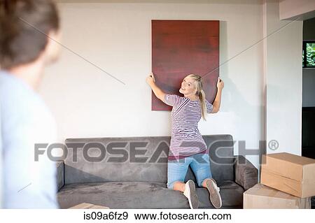 Young couple moving house, woman hanging painting View Large Photo Image Stock Photo - Young couple moving house, woman hanging painting. Fotosearch