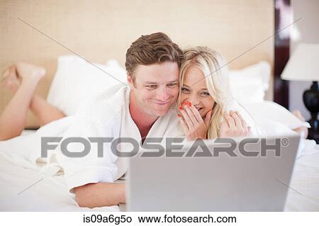 Picture - Young couple on bed using laptop. Fotosearch