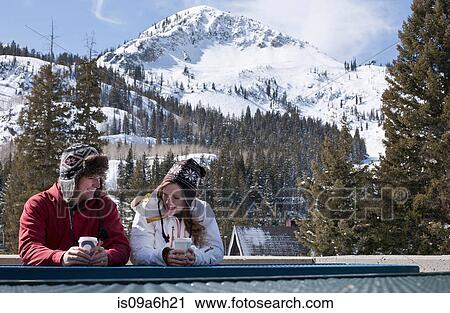 Stock Image - Young couple with hot drinks in Brighton ski resort, Utah, USA. Fotosearch