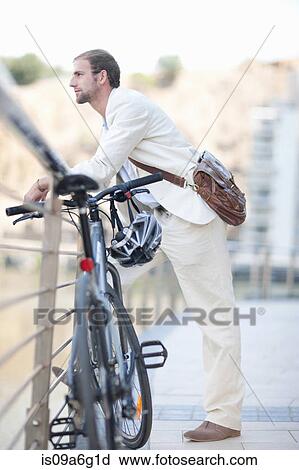 Stock Image - Young man by railings with bicycle. Fotosearch