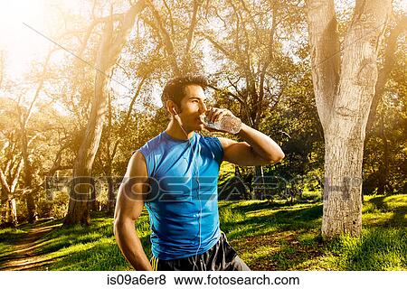 Stock Photo - Young man exercising in forest drinking mineral water. Fotosearch