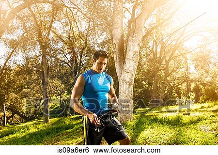 Stock Photograph - Young man exercising in forest holding earphones. Fotosearch