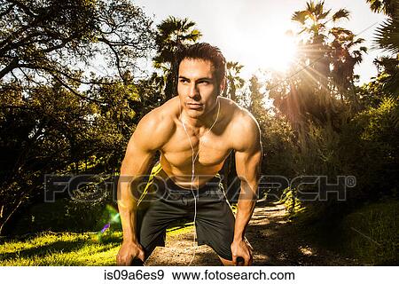 Stock Photo - Young man exercising in forest resting. Fotosearch