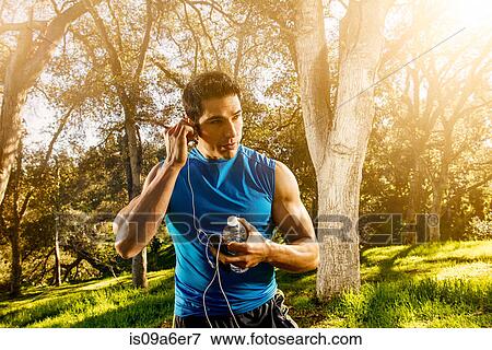 Stock Photo - Young man exercising in forest wearing earphones. Fotosearch