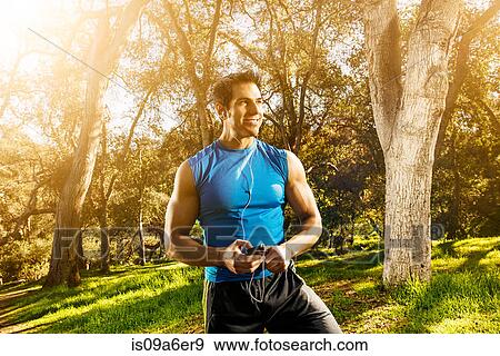Stock Photo - Young man exercising in forest wearing earphones. Fotosearch