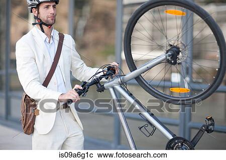 Stock Image - Young man lifting bicycle. Fotosearch