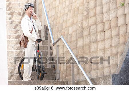 Young man on steps on cell phone with bicycle View Large Photo Image Stock Photograph - Young man on steps on cell phone with bicycle. Fotosearch