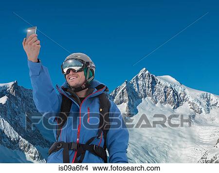 Picture - Young man photographing self on smartphone in mountains. Fotosearch