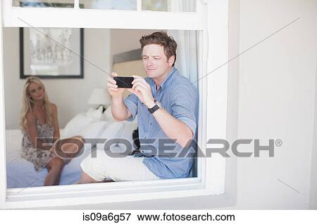Stock Photo - Young man taking photograph through window with smartphone. Fotosearch