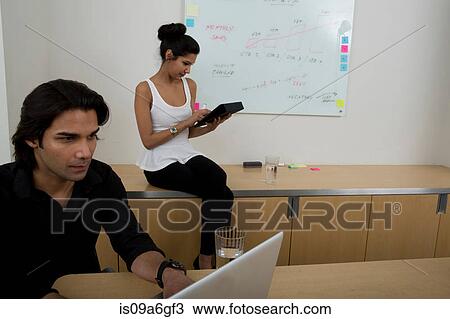 Young man using laptop with woman in background View Large Photo Image Stock Image - Young man using laptop with woman in background. Fotosearch