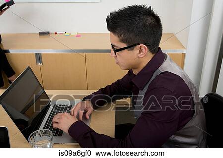 Stock Image - Young man wearing glasses using laptop. Fotosearch